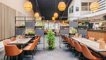 A modern restaurant with high tables, orange chairs, and hanging wicker lamps.
