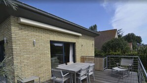 A patio with a table and chairs, a sliding glass door, and a wooden deck. - Villa in Oostduinkerke Near Dunes (Koksijde)