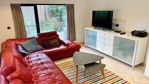 A modern living room with a red leather sofa, a small table, a white cabinet with a television and stereo equipment, and a striped rug. - Villa in Oostduinkerke Near Dunes (Koksijde)