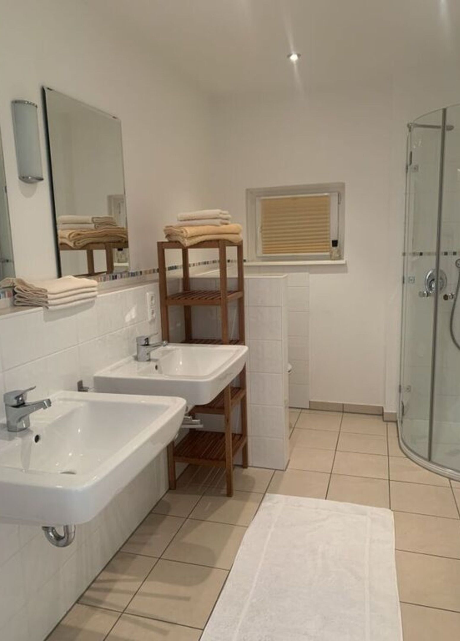 Ein Badezimmer mit zwei Waschbecken, einer Holzablage, einem Spiegel und einer Duschkabine aus Glas.