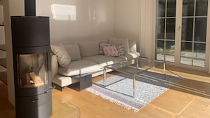Ein modernes Wohnzimmer mit einem Glastisch, einem beigefarbenen Sofa und einem Kaminofen.