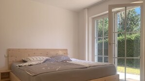 Ein Schlafzimmer mit einem hölzernen Bett, einem Nachttisch und einem großen Fenster mit Blick auf Grünfläche.