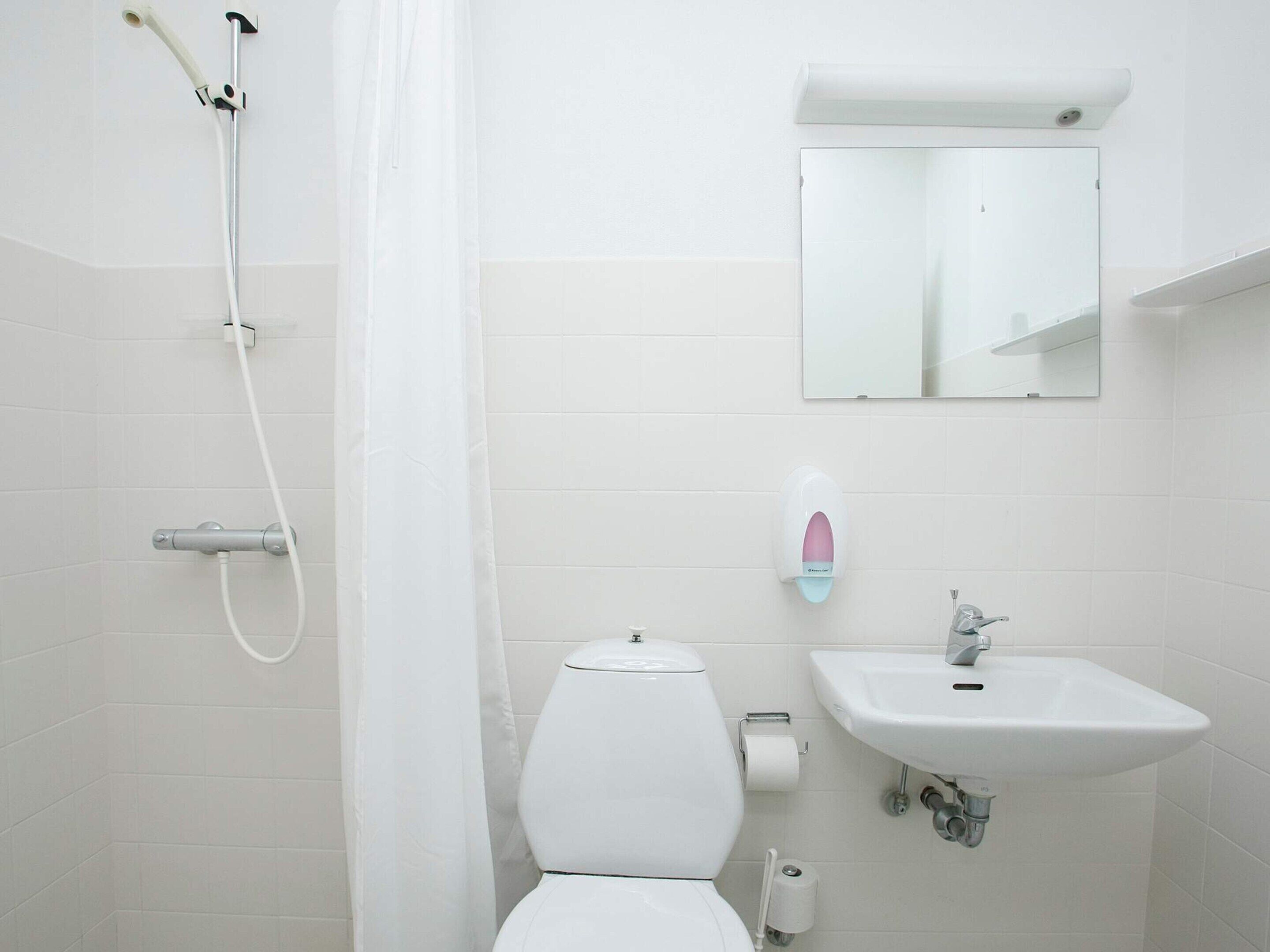 Et badeværelse med brusebad, toilet, vask og spejl.