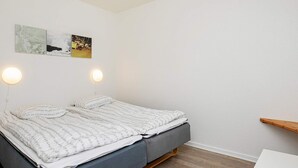 A neatly made bed with a grey mattress and white bedding, two wall-mounted round lights, and a wooden shelf against a white wall. - 4 Person Holiday Park Home in Hanstholm (Hanstholm)
