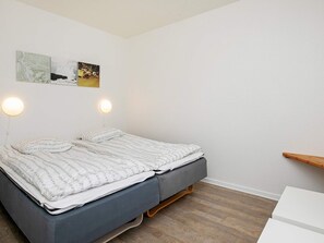 A neatly made bed with a grey mattress and white bedding, two wall-mounted round lights, and a wooden shelf against a white wall. - 4 Person Holiday Park Home in Hanstholm (Hanstholm)