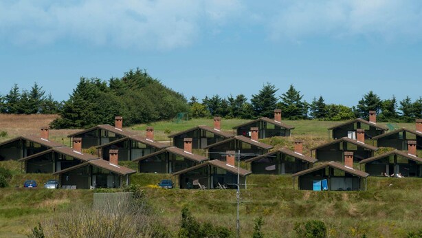 A row of modern, single-story cabins with sloped roofs, set in a grassy field with trees in the background. - 4 Person Holiday Park Home in Hanstholm (Hanstholm)