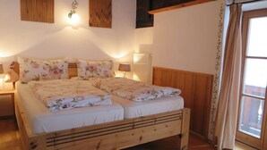 A double bed with floral bedding, wooden headboard, bedside lamps, and a window with curtains. - Nagelsmederij in het Huis Waldwinkel (Aschau im Chiemgau)