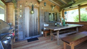 A rustic cabin interior with wooden walls, a wooden ceiling, a dining table with benches, and a grill. - Nagelsmederij in het Huis Waldwinkel (Aschau im Chiemgau)