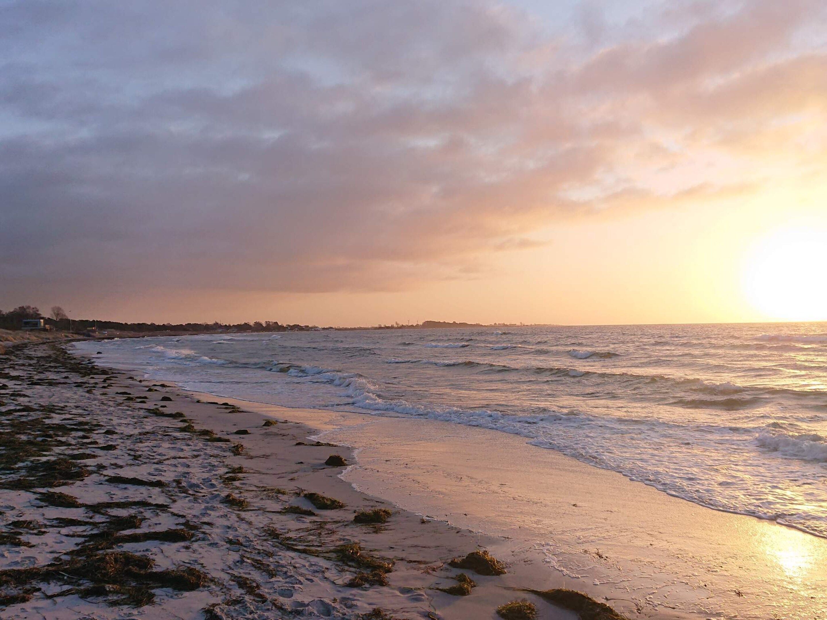 A beach with waves, a sunset, and a distant shoreline.