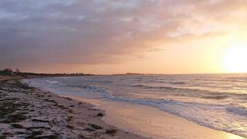 A beach with waves, a sunset, and a distant shoreline.