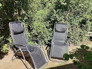 Deux fauteuils de jardin, avec une structure en métal et des assises en toile, sont placés sur une pelouse, avec un feuillage dense en arrière-plan.