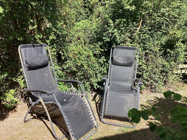 Two outdoor lounge chairs with metal frames and canvas seats, positioned on a grassy area with dense foliage in the background. - 4 Person Holiday Home in Hollviken (Hollviken)