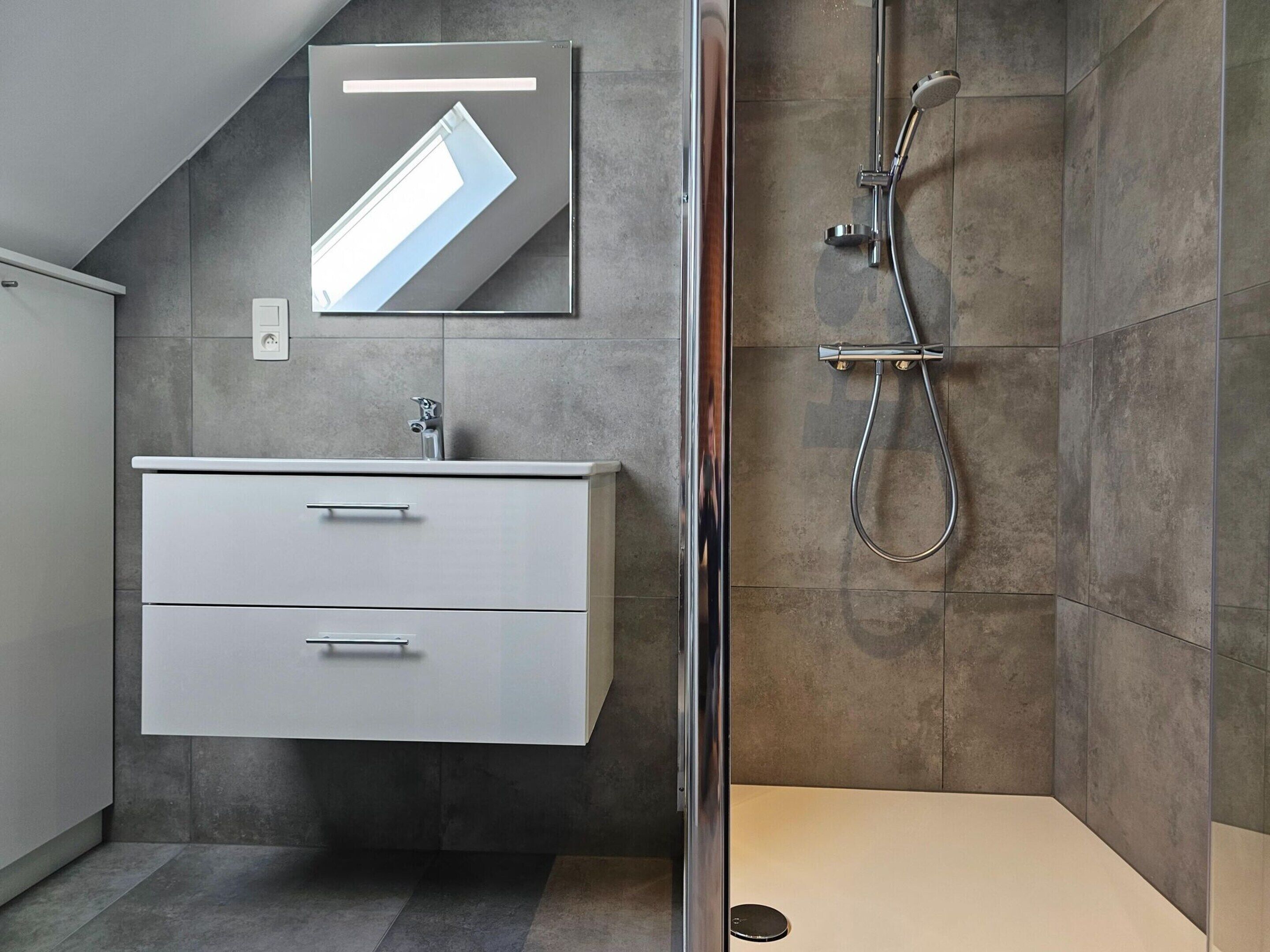 A modern bathroom with a vanity, a shower with a handheld showerhead, and a large mirror.