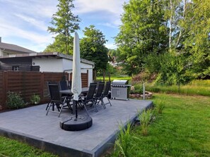 An outdoor patio with a table and chairs, a barbecue grill, and a covered umbrella.