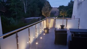 An outdoor patio with a railing, potted plants, and string lights. - Holiday House on Bornfeld (Leimen)