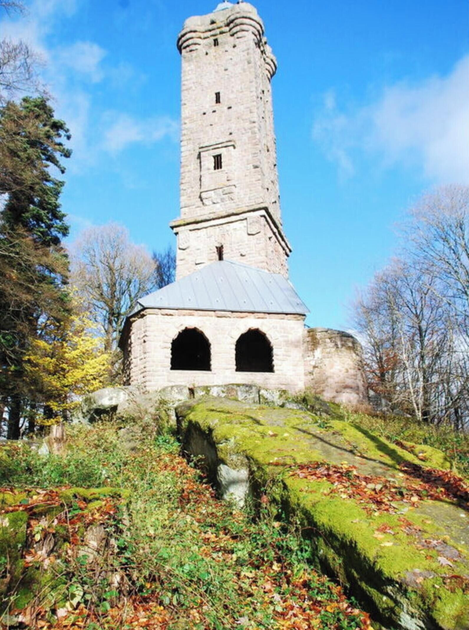 A stone tower with a conical roof, surrounded by autumn foliage and trees.