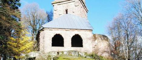 A stone tower with a conical roof, surrounded by autumn foliage and trees.