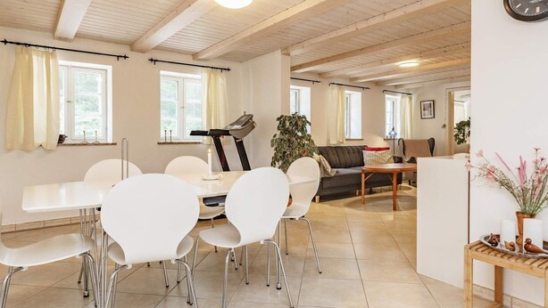 A spacious living area with a dining table, white chairs, a treadmill, and a sofa. - 6 Person Holiday Home in Rodby (Rodby)