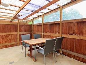 Un patio al aire libre con una mesa y sillas de madera, rodeado de paredes de madera y un techo de metal.