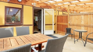 A wooden patio with a table and chairs, a glass door, and a wooden fence. - 6 Person Holiday Home in Rodby (Rodby)