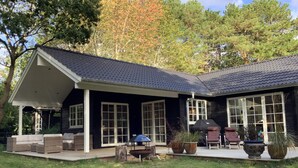 Ein Haus mit überdachter Terrasse, großen Fenstern und Sitzgelegenheiten im Freien.