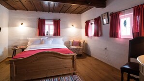 Quarto com cama de madeira, duas mesas de cabeceira, uma cadeira e uma escrivaninha.