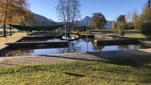 Um parque tranquilo com um pequeno lago, pontes de madeira e uma montanha ao fundo.