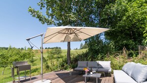 Um deck externo com um sofá, uma mesa e um guarda-sol.