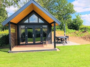 A modern, single-story building with a sloped roof, large glass doors, and a patio area with outdoor seating. - Chalet in Netherlands With Dual Terraces (Lathum)