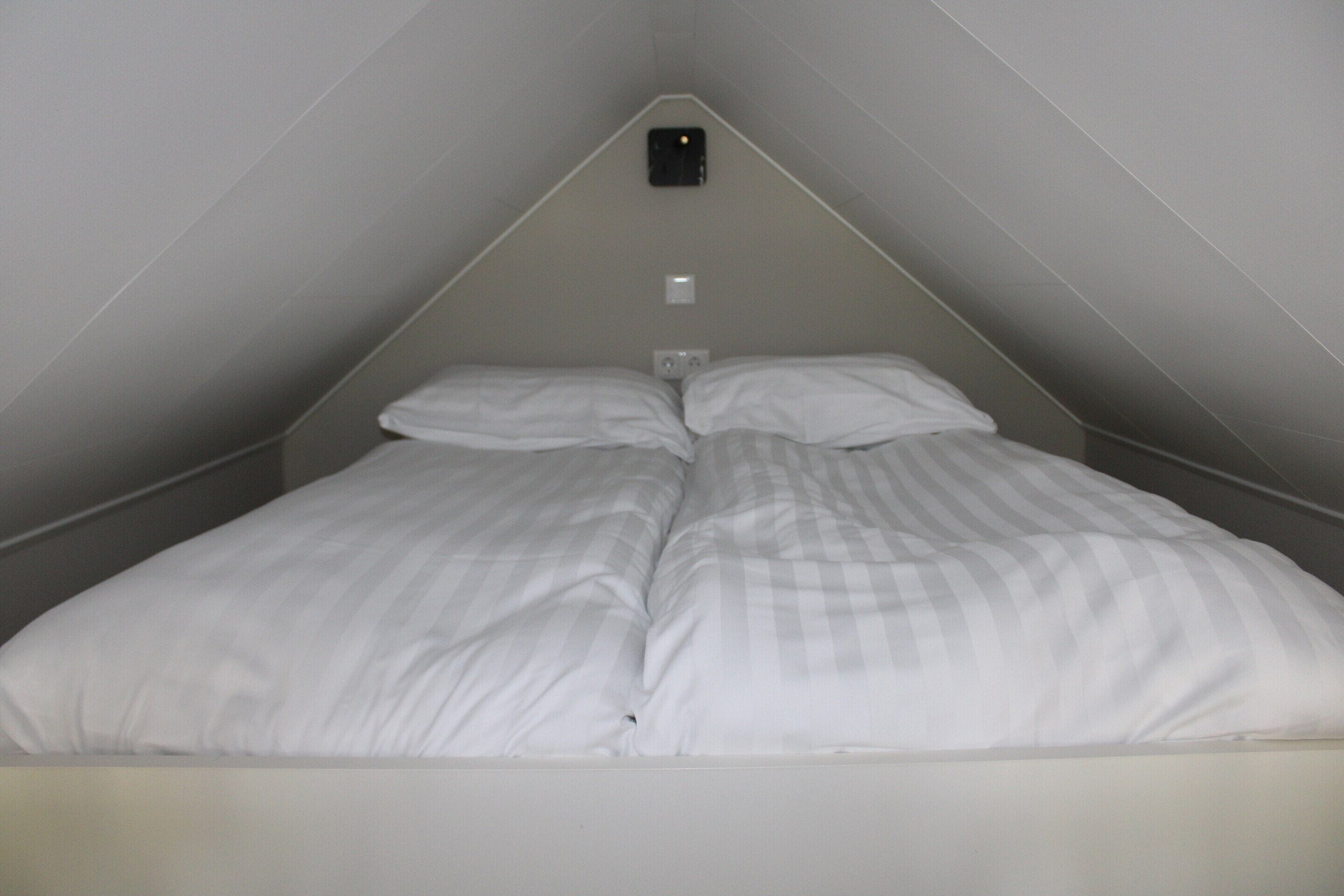 A small, triangular room with a single bed and a wall-mounted light fixture.