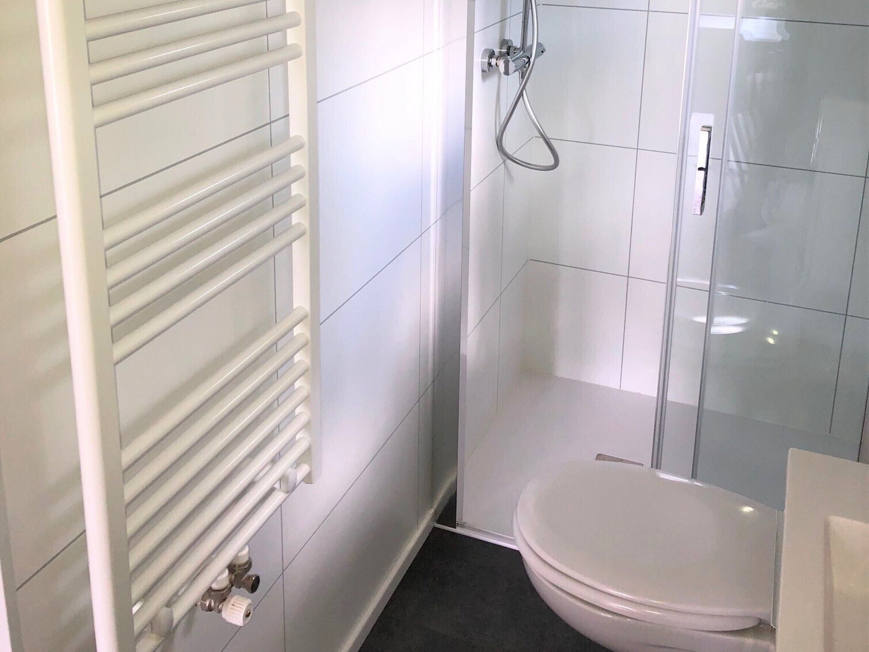 A modern bathroom with a glass shower enclosure, a toilet, and a radiator.