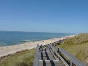Une promenade en bois menant à une plage où se trouvent des tentes et des parasols.