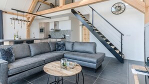 A modern living room with a grey sectional sofa, a round wooden coffee table, and a staircase with a wooden railing. - Chic Thatched-roof Stay (Baarle-Nassau)