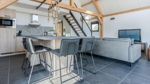 A modern kitchen with a central island, bar stools, and a staircase leading to an upper level. - Chic Thatched-roof Stay (Baarle-Nassau)