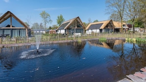 A tranquil outdoor setting with a pond, wooden buildings with thatched roofs, and a clear blue sky. - Chic Thatched-roof Stay (Baarle-Nassau)
