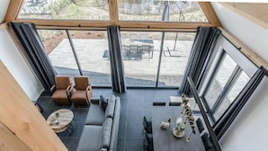 A high-ceilinged room with a view of an outdoor patio, featuring a sofa, chairs, and a dining table. - Chic Thatched-roof Stay (Baarle-Nassau)