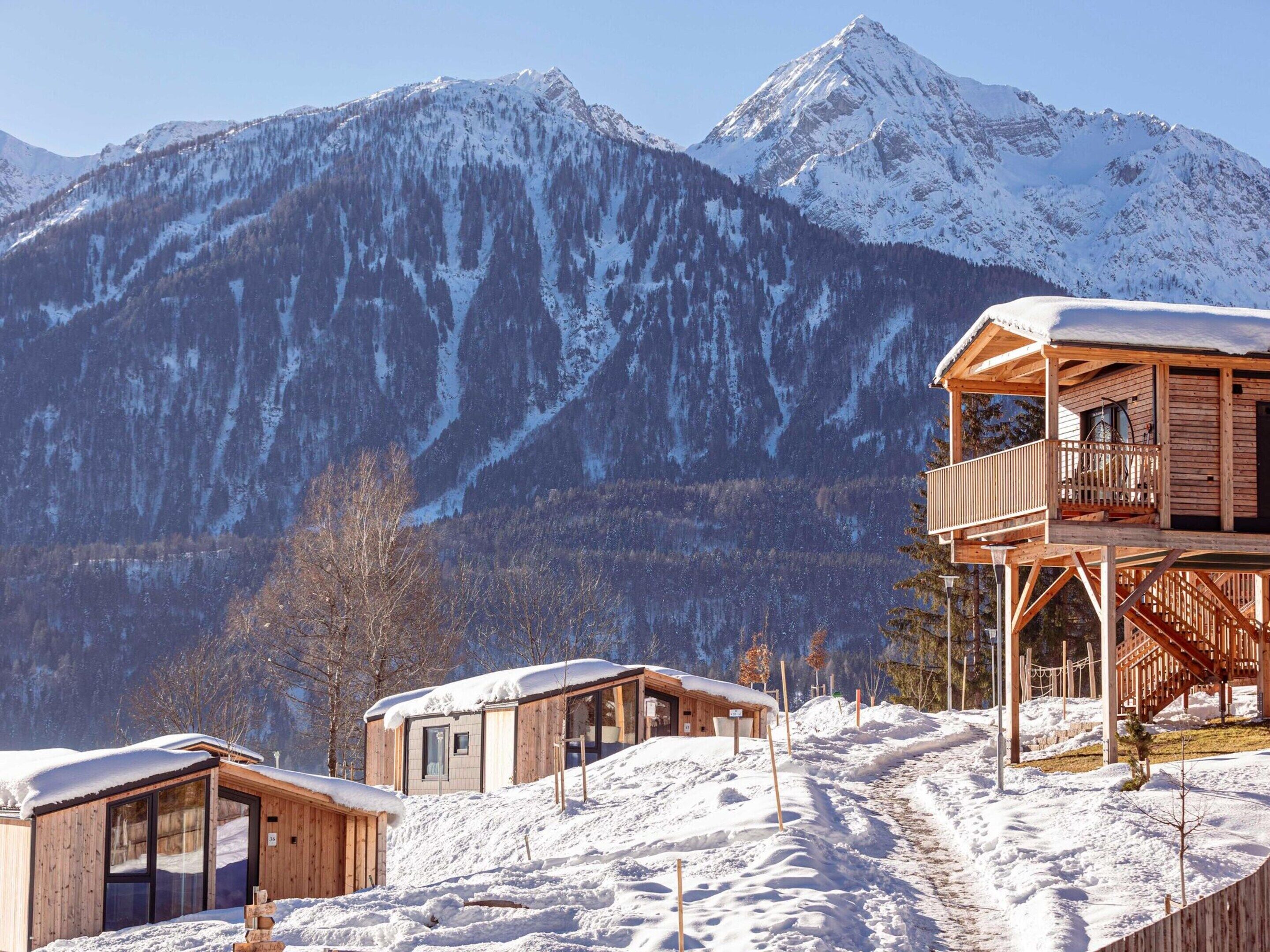A wooden cabin with a balcony, surrounded by snow-covered mountains.