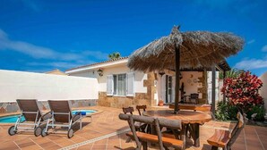 Eine Terrasse mit Pool, Holzmöbeln und einem Reetdachschirm.