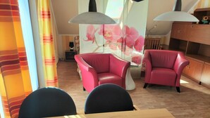 A dining area with a wooden table and two red chairs, a glass-top table, and a floral wall mural. - Apartment in Neu Ludershagen With Terrace (Wendorf)