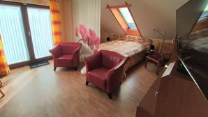 A bedroom with a large bed, two red armchairs, a TV, and a skylight. - Apartment in Neu Ludershagen With Terrace (Wendorf)