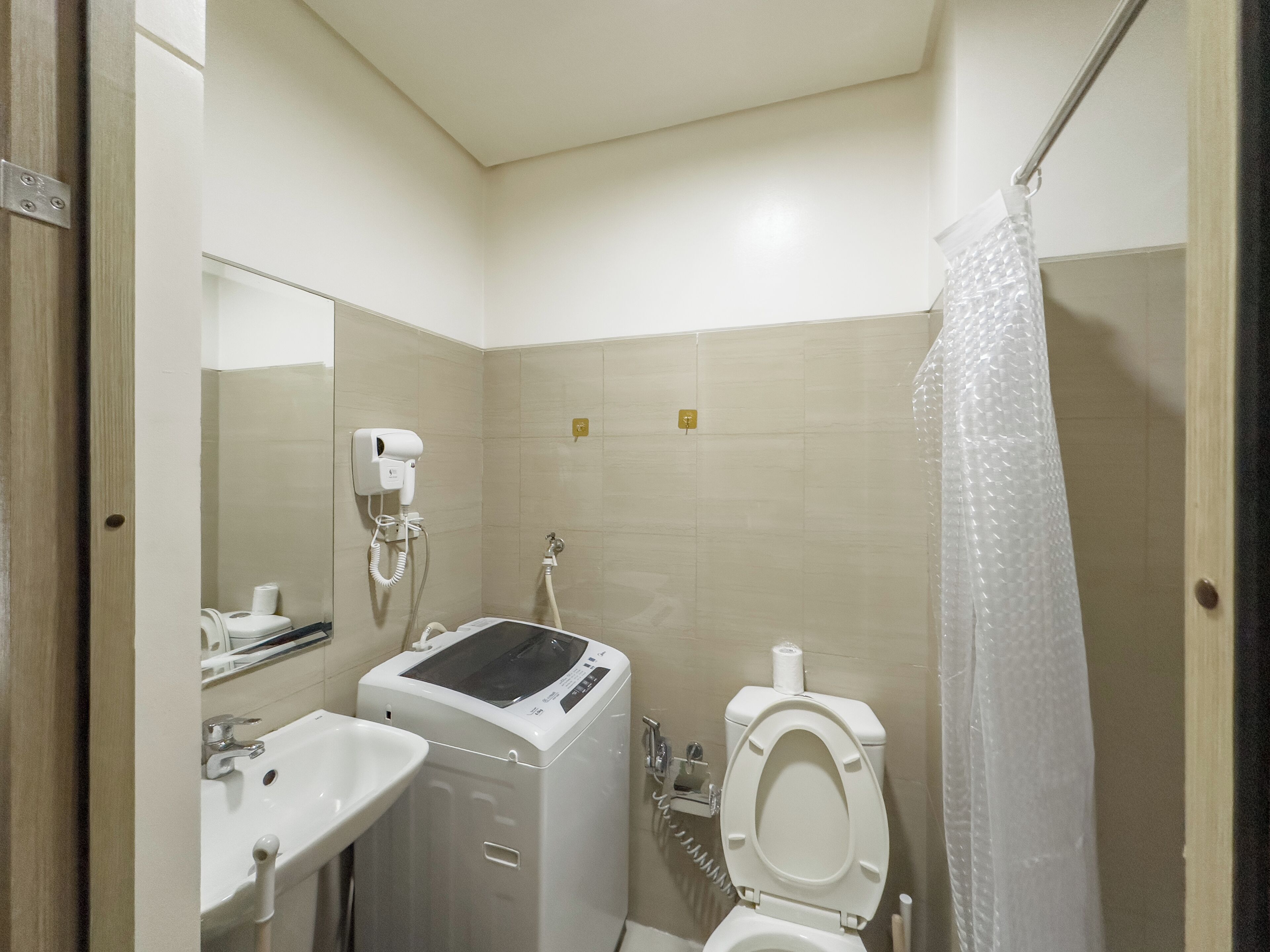 A small bathroom with a sink, a hairdryer, a toilet, and a shower curtain.