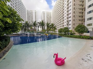 Une piscine avec un flotteur en forme de flamant rose, entourée de verdure et de grands immeubles.