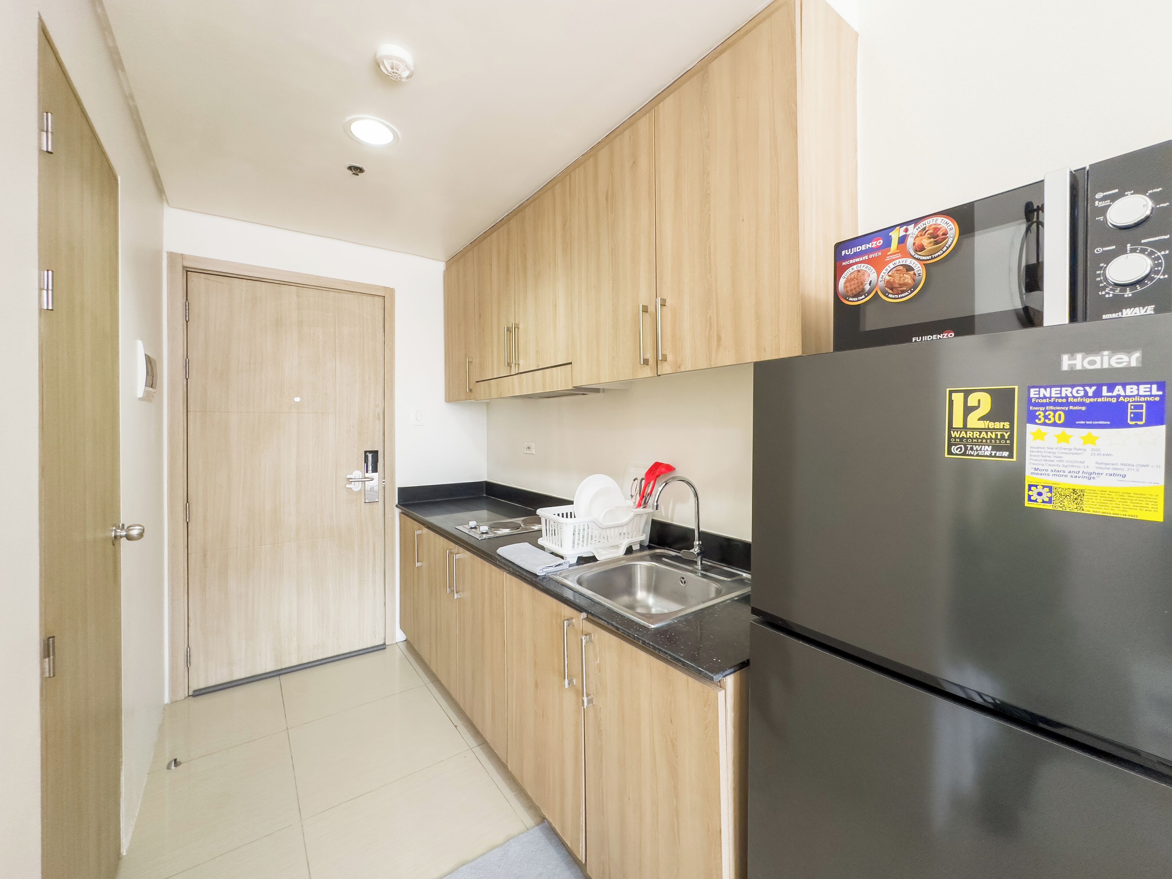 A compact kitchen with wooden cabinets, a stainless steel sink, and a black refrigerator with an energy efficiency label.