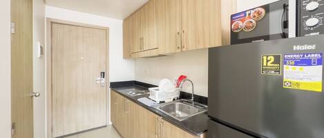 A compact kitchen with wooden cabinets, a stainless steel sink, and a black refrigerator with an energy efficiency label.