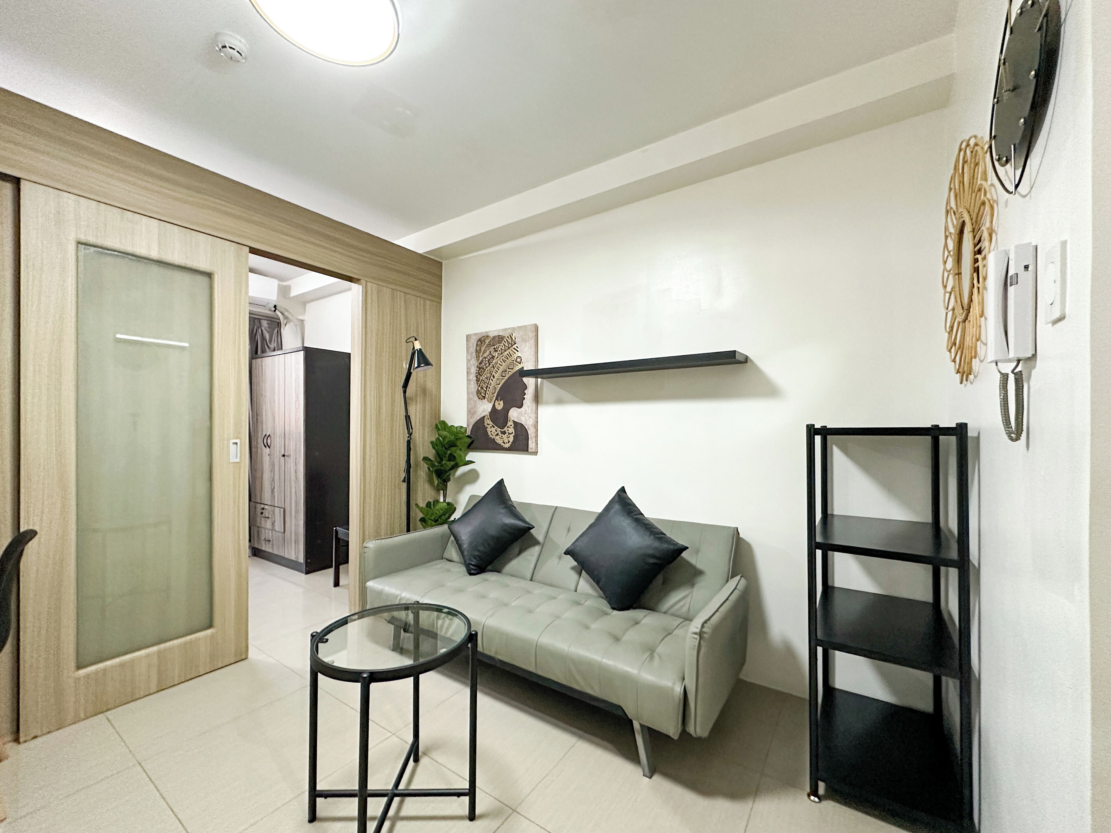 A modern living room with a sofa, a glass coffee table, and a black shelving unit.