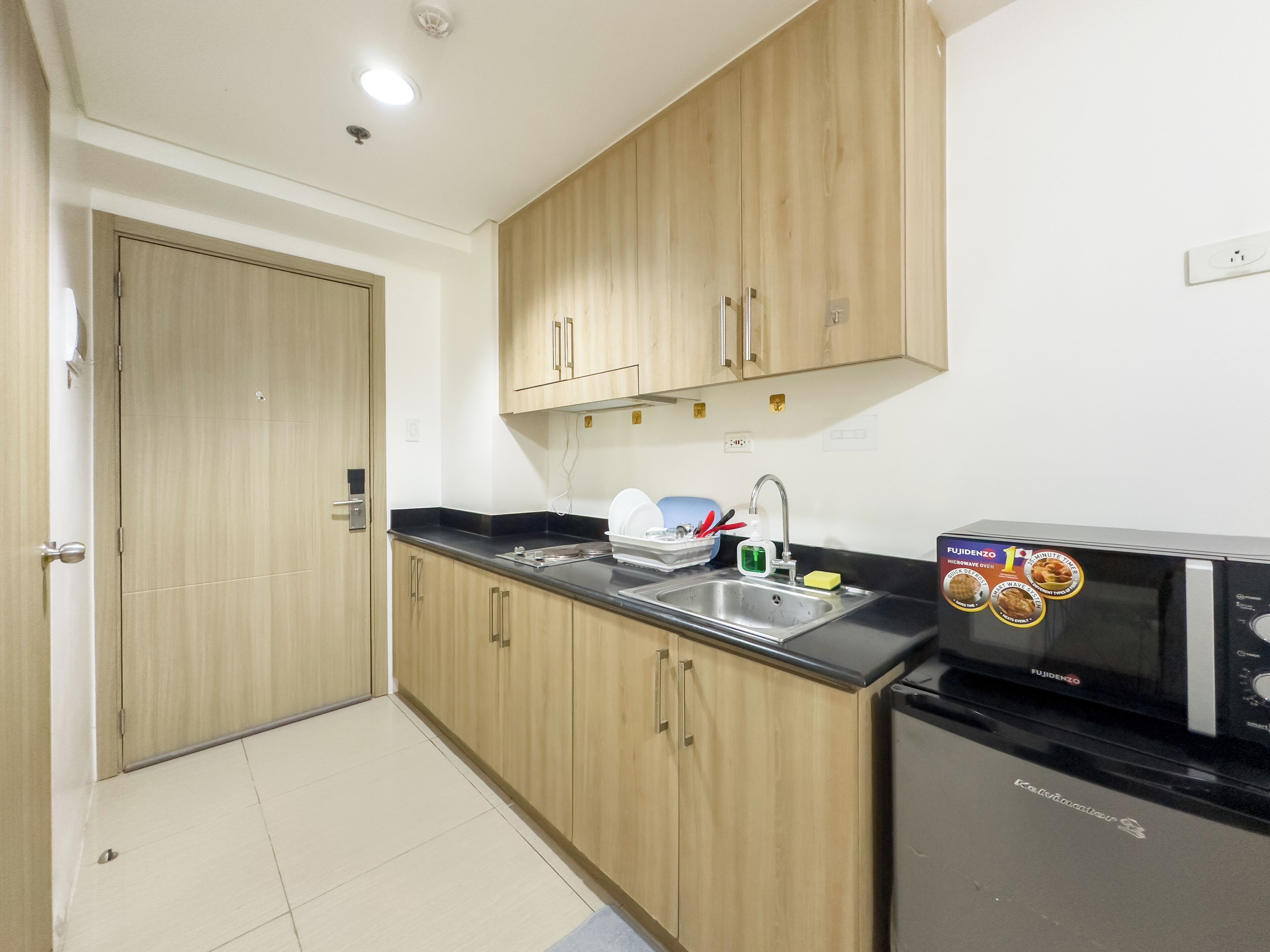 A compact kitchen with wooden cabinets, a black countertop, a sink, and a black microwave.