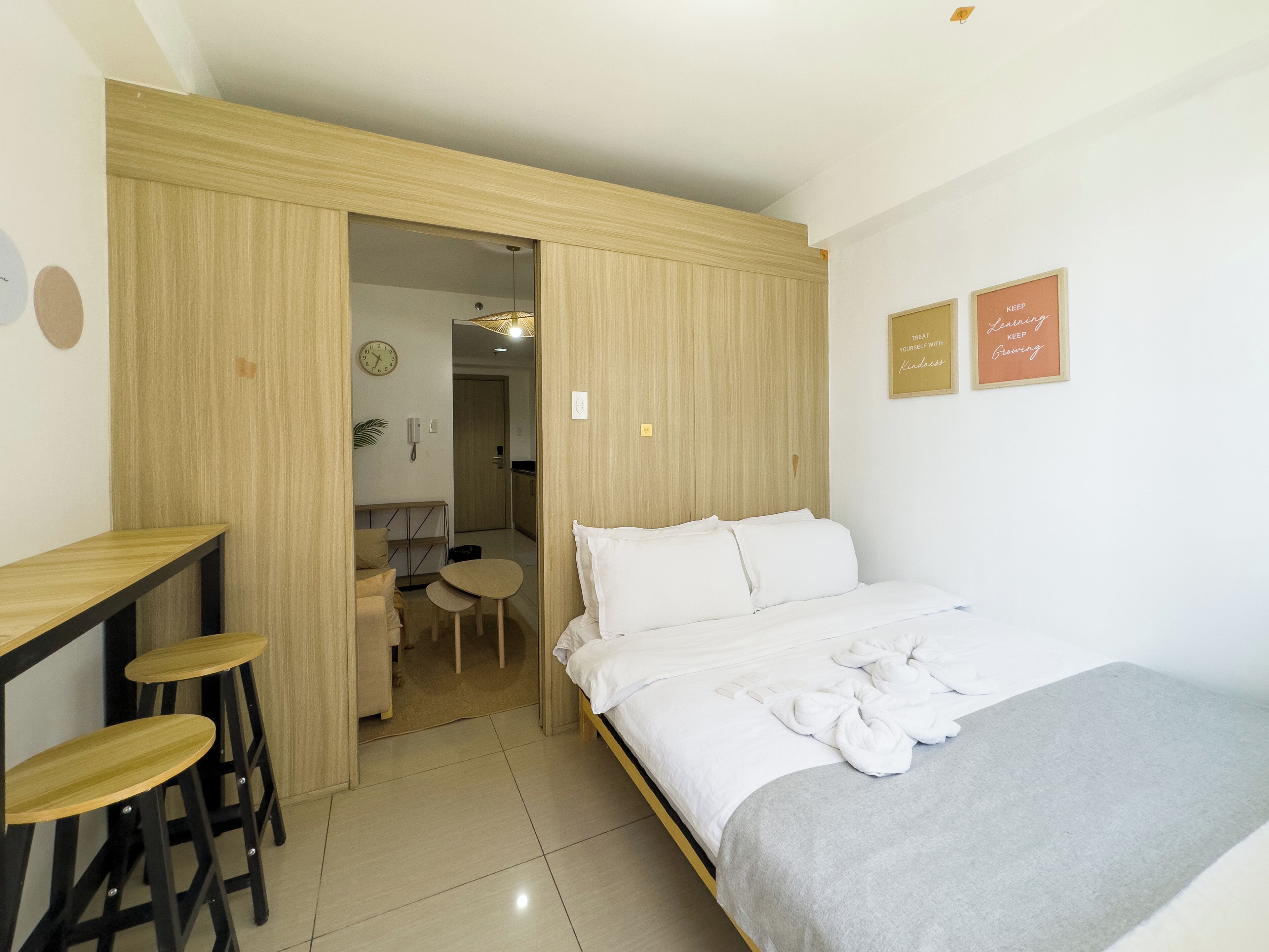 A bedroom with a bed, a desk with stools, a small table, and a door leading to a bathroom.
