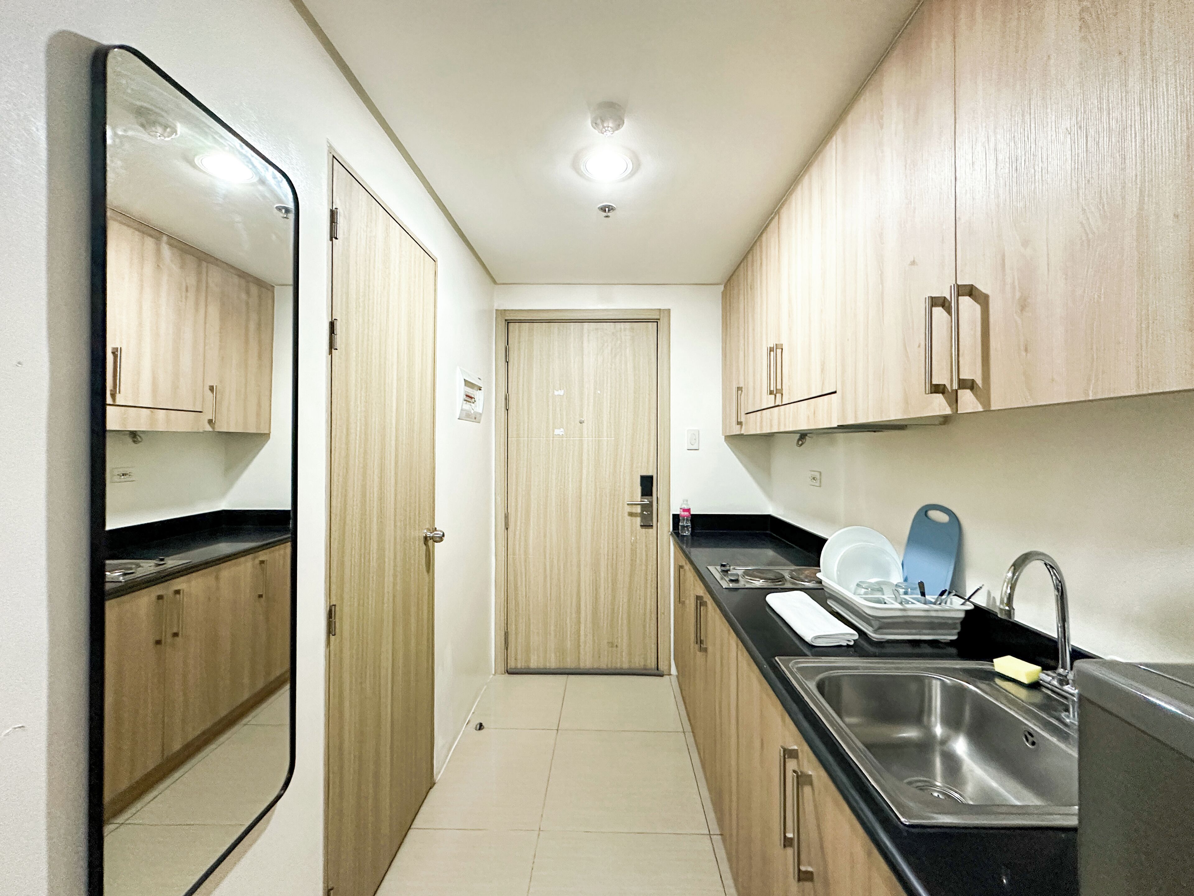 A narrow kitchen with wooden cabinets, a stainless steel sink, and a black countertop.