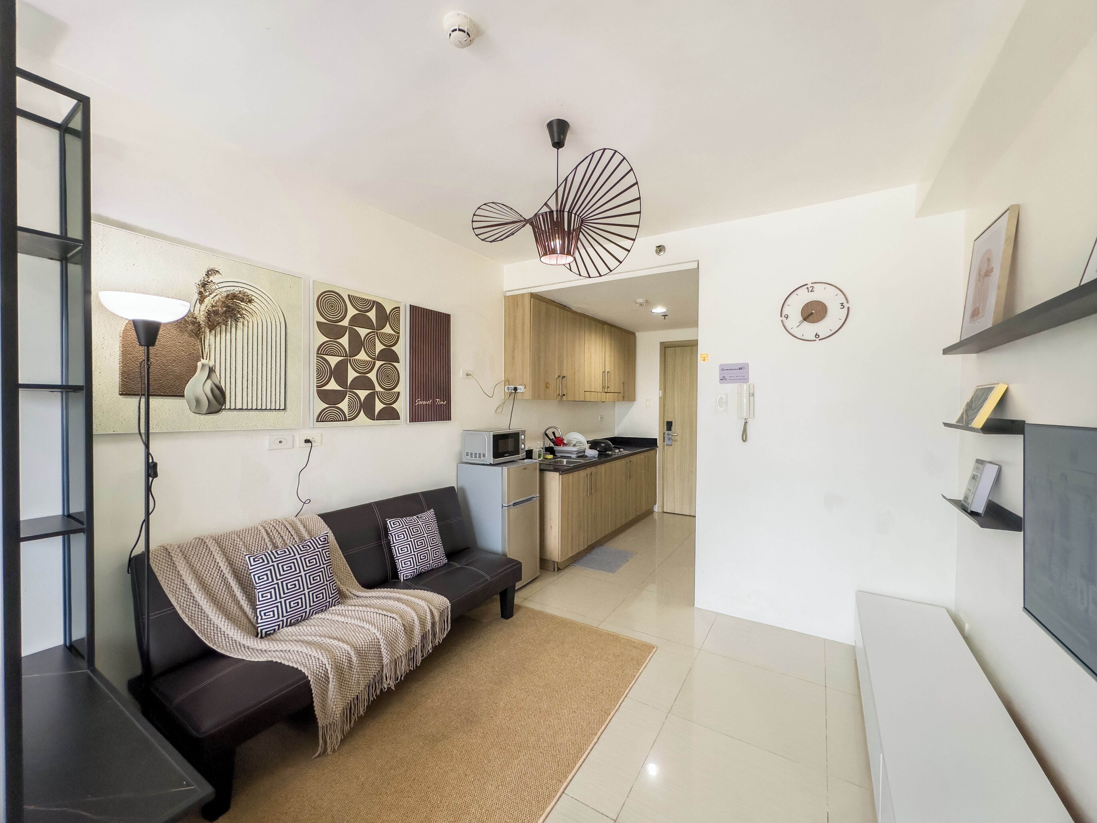 Uma sala de estar moderna com um sofá preto, uma mesa de centro e um espaço de refeições com micro-ondas e armários.