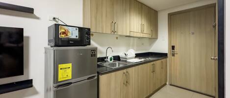 A compact kitchen with a refrigerator, microwave, sink, and wooden cabinets.